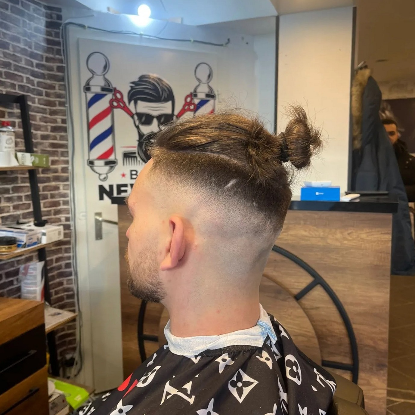 Fade met een knot bovenop, met de barberpaal op de muur erachter