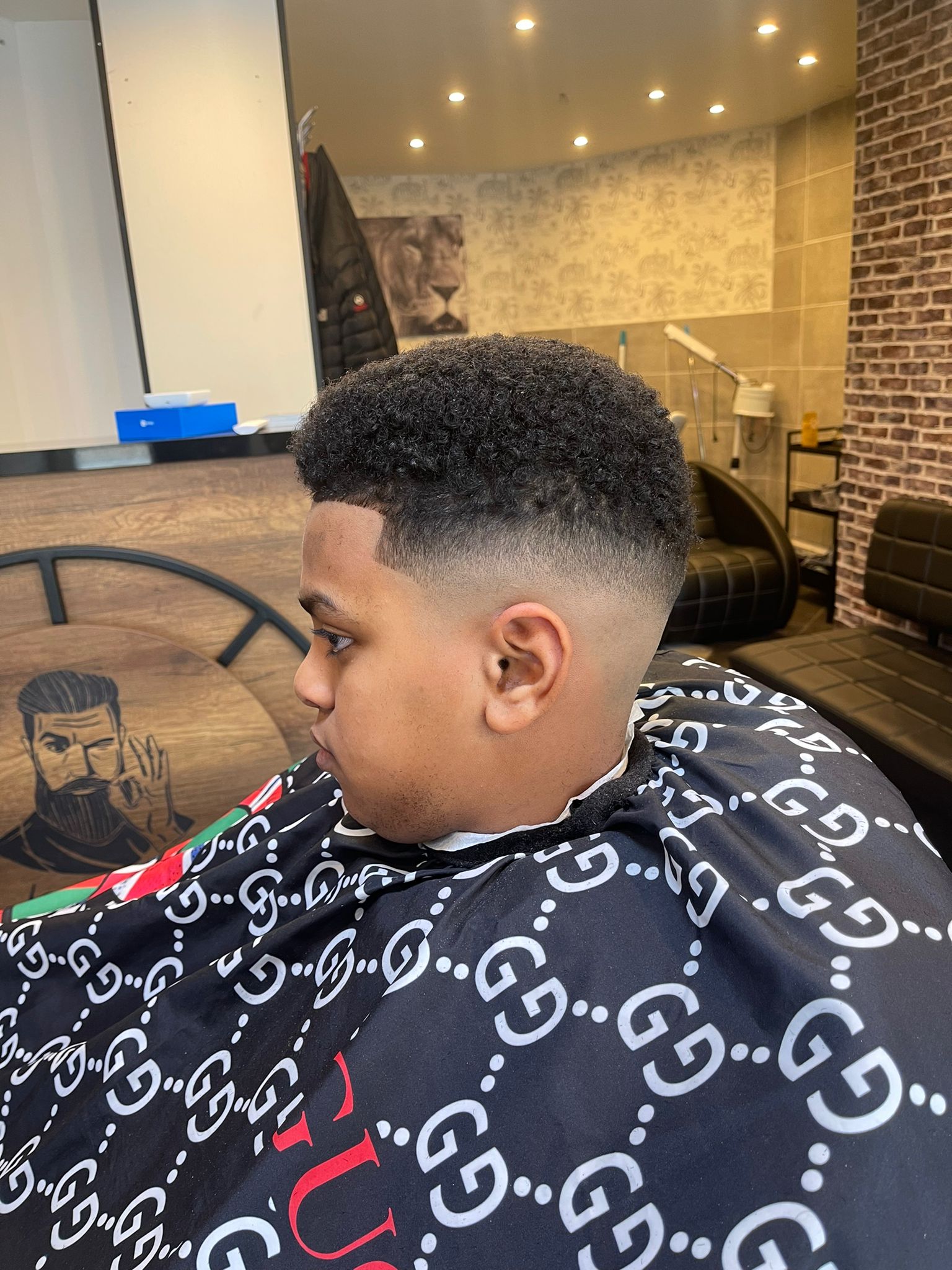 Jonge klant met een fade, kort aan de zijkant en krullen bovenop, in de stoel bij Barber Newstar